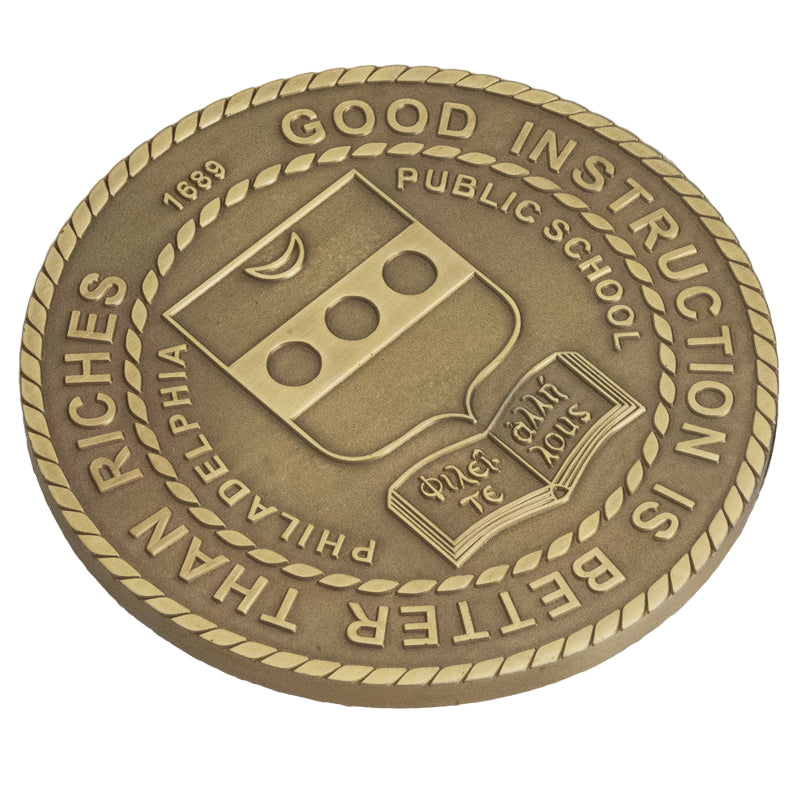 An antiqued brass coaster featuring a Philadelphia Public School logo, surrounded by a rope border.