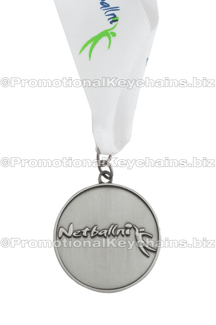 An antiqued nickel netball medal featuring the logo for "Netballni". It's attached to a white ribbon with a custom imprint of the same logo that is on the medal itself.