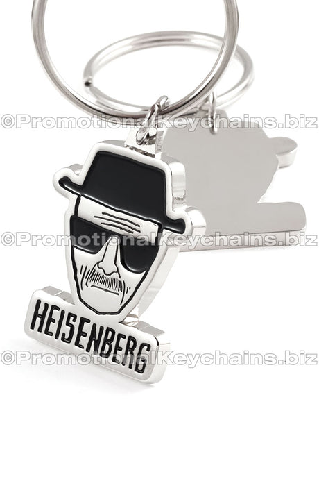 The front and back of polished nickel keychain featuring a stylized head with a hat and the name "HEISENBERG" in black enamel color underneath. The back side has a smooth, shiny finish.