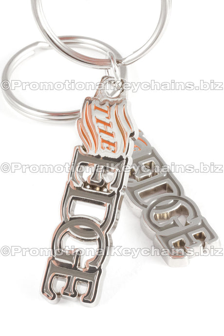 Two angles of the same polished nickel keychain featuring the words "THE EDGE" in orange and gray enamel color.