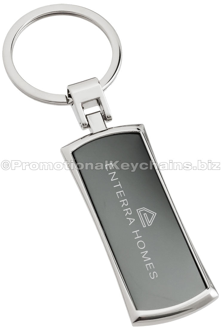 A polished metal rectangular keychain featuring a black metal inlay with "Enterra Homes" engraved in the center.