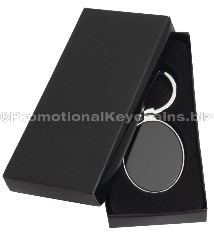 A polished metal keychain with an oval black center displayed in a black gift box.