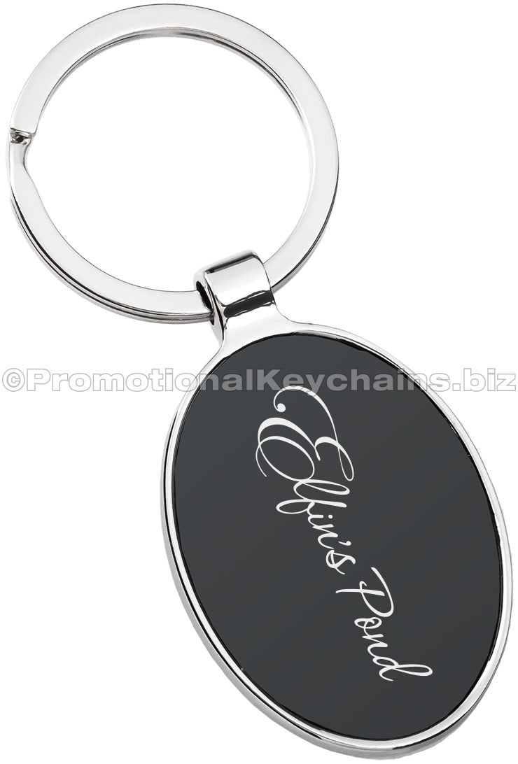 A polished metal keychain with an oval black center featuring engraved script text.