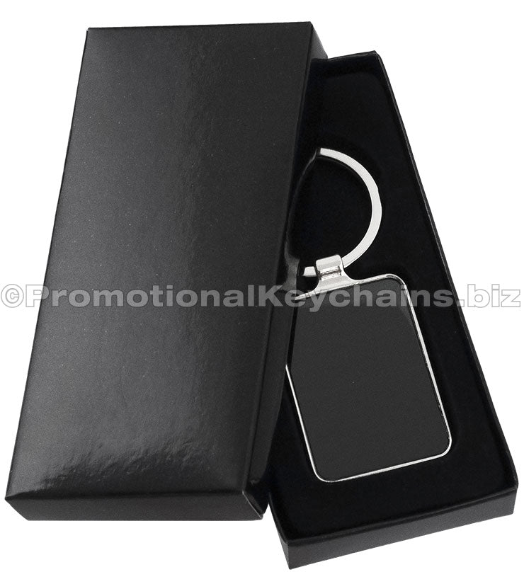 A polished metal keychain featuring a black rectangular background displayed in a black gift box.