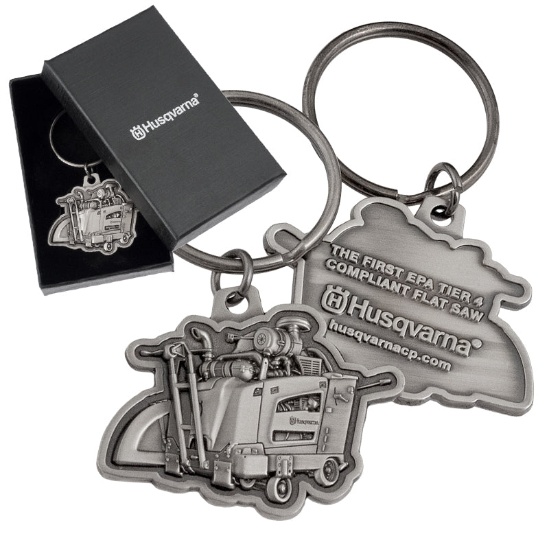 Both sides of an antiqued nickel keychain featuring a detailed, 3-dimensional flat saw design and text embossed on the back side. There is also an image of the same keychain inside of a black gift box, and the lid of the box has a customized silver imprint.