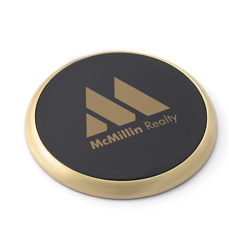 A brass coaster with a black leather center that is imprinted with the McMillin Realty logo.