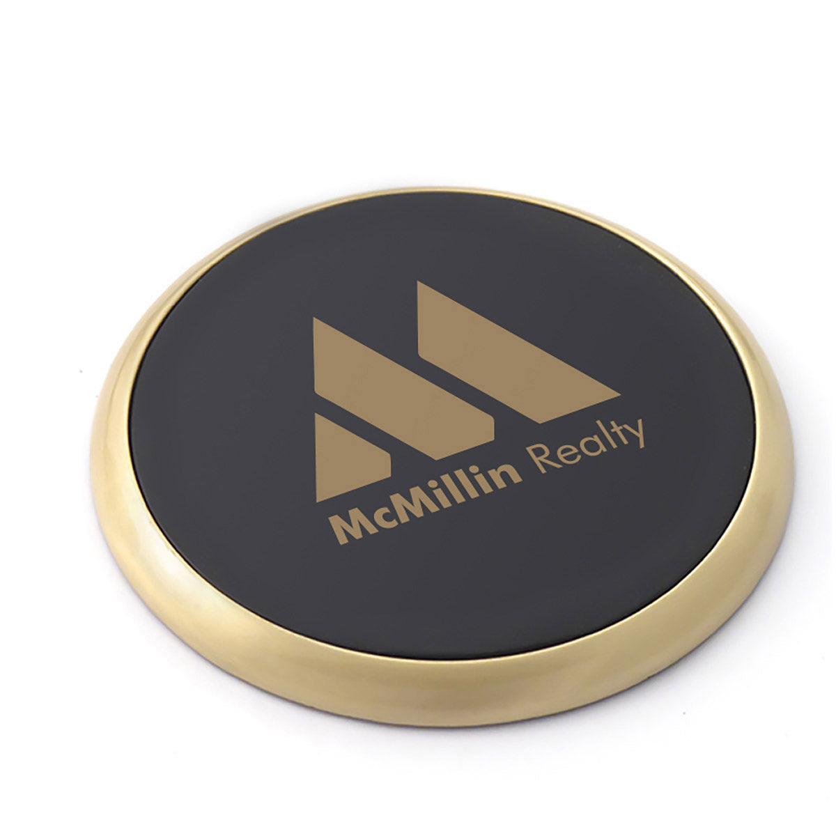 A brass coaster with a black leather center that is imprinted with the McMillin Realty logo.