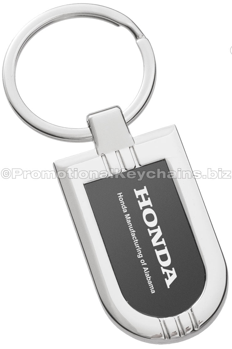 A polished metal badge keychain featuring a black metal inlay with an engraving of the Honda logo.