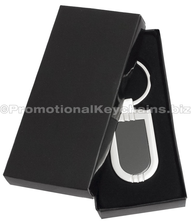 A polished metal badge keychain featuring a black metal inlay displayed in a black gift box.