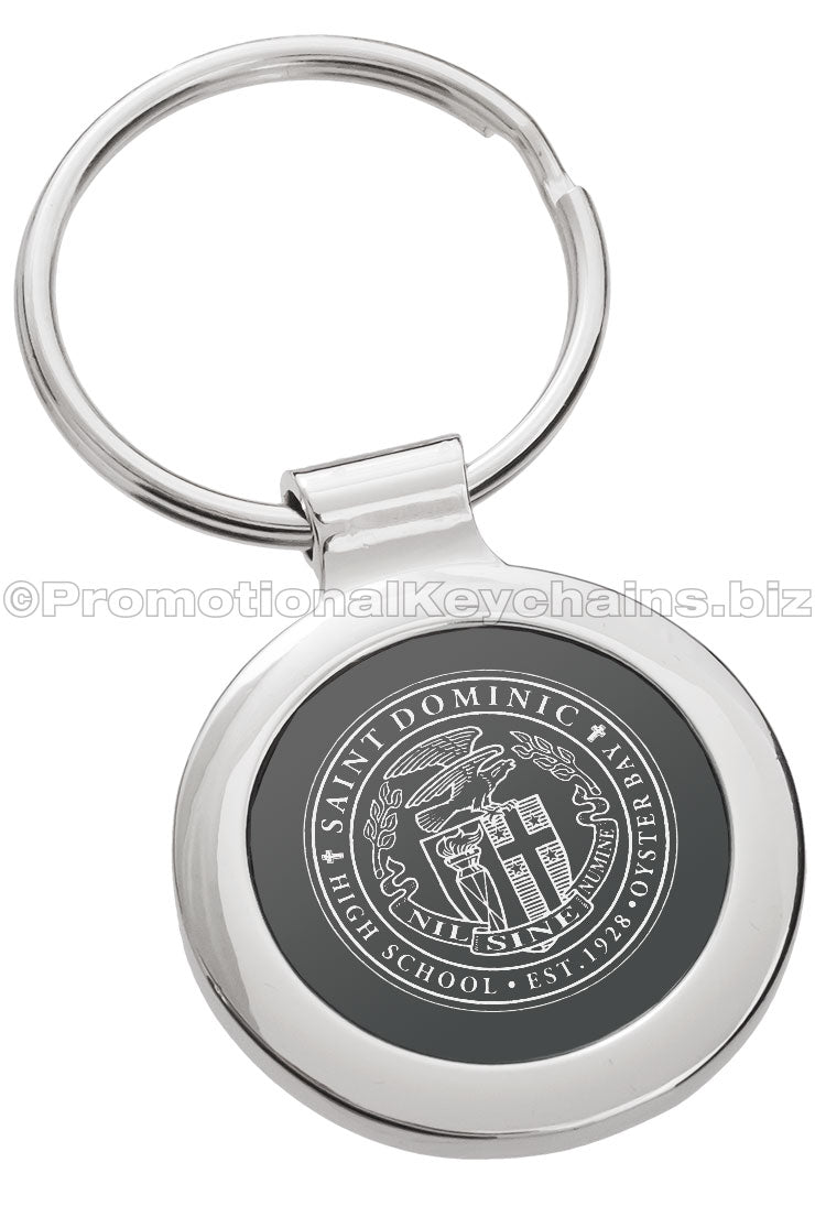 A circular polished metal keychain featuring a black inlay and a finely detailed logo engraved in the center.