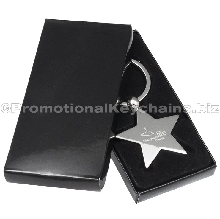 A polished metal star-shaped keychain featuring an engraved logo, displayed in a black gift box.