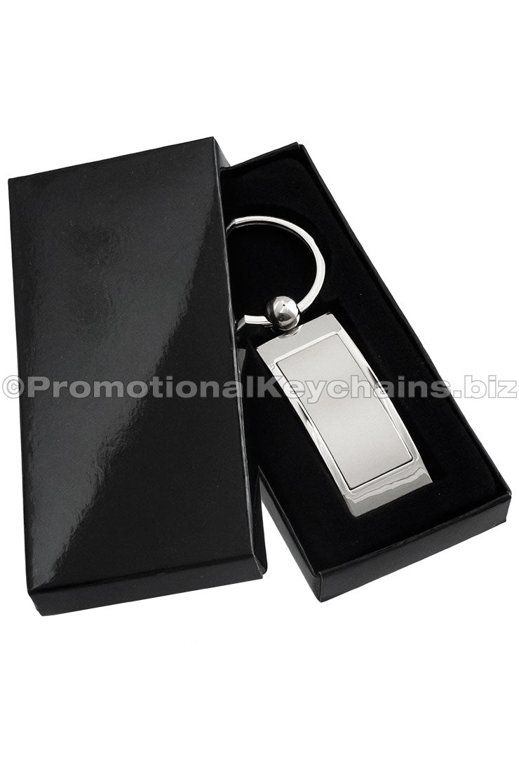 A polished metal keychain, rectangular in shape, displayed in a black gift box.