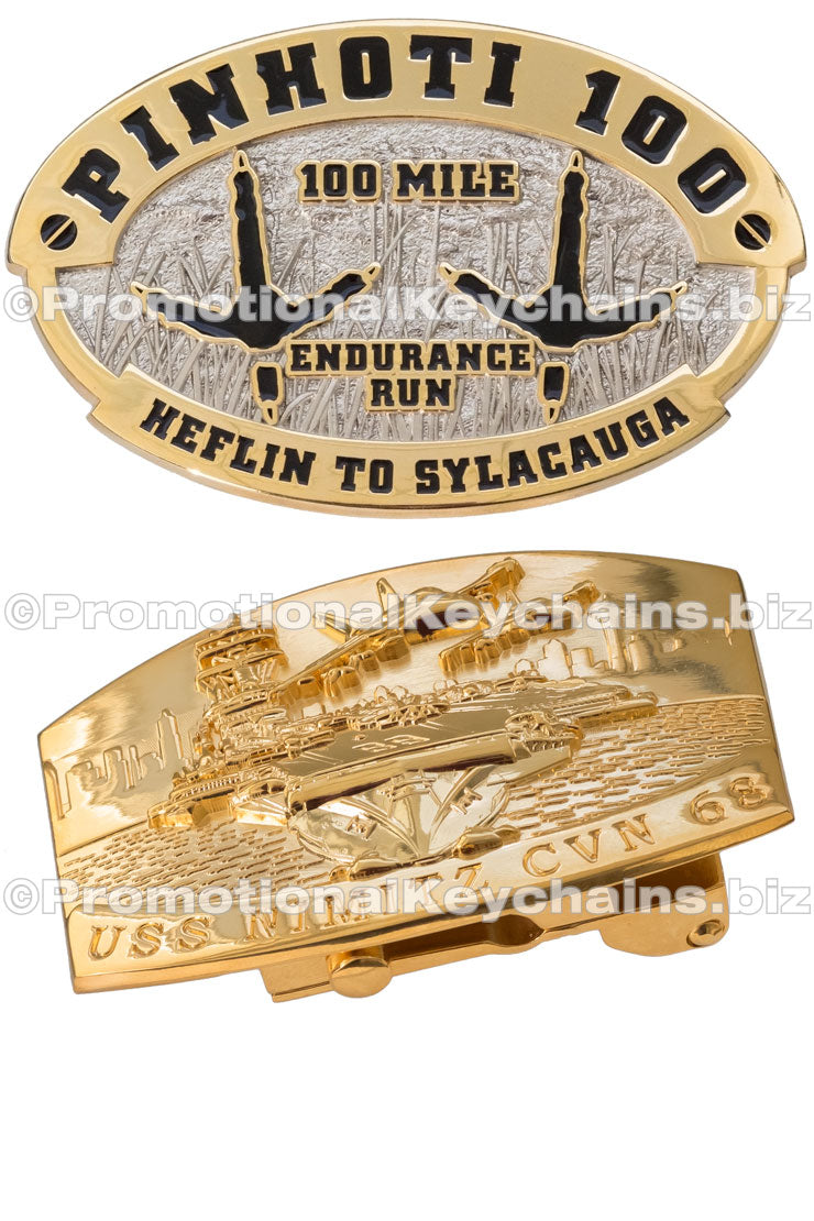 Two different polished belt buckles are shown. One is dual-plated in nickel and gold with the outline of two avian footprints in the center. The other is entirely in polished gold with a prominent 3-dimensional tank design.