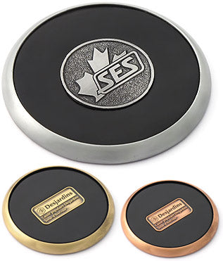 Three coasters are shown. On the top, an antique nickel design with the "SES" logo molded into a round medallion and inlayed in the center, surrounded with black leather. The bottom coasters are built similarly except with a rectangular medallion in the center and are instead plated in brass and copper.
