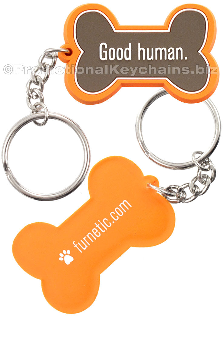 Both sides of a bright orange PVC keychain shaped like a dog bone and featuring the text "Good human." on the front. On the back, "furnetic.com" is screen printed in white.
