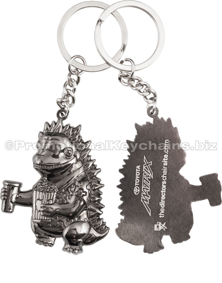 Both sides of a polished keychain featuring a 3-dimensional cartoon dinosaur holding popcorn and a drink on the front and a screen printed white imprint on the back.