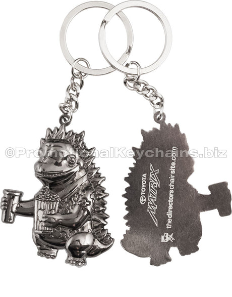 Both sides of a polished keychain featuring a 3-dimensional cartoon dinosaur holding popcorn and a drink on the front and a screen printed white imprint on the back.
