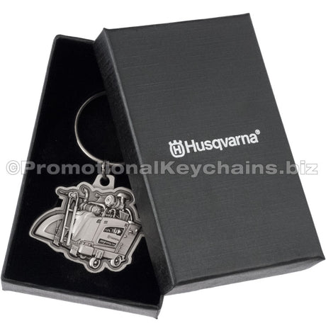 An antiqued nickel keychain featuring a detailed, 3-dimensional flat saw design placed into a black gift box. The lid of the box is visible to the side and has a custom silver imprint on the center.