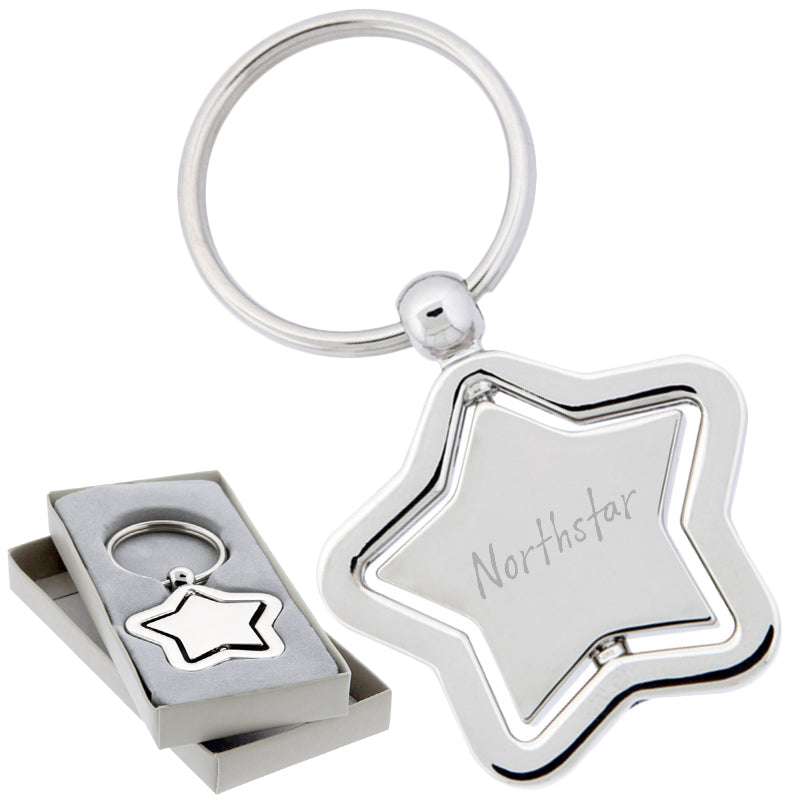 There are two images. On the left, a polished metal star-shaped keychain with a spinning center. It is displayed in a grey gift box. On the right is the same keychain with a logo clearly engraved in the center.