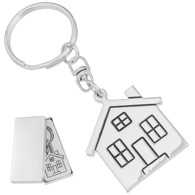 There are two images. On the left, a polished metal house-shaped keychain displayed in a silver gift box. On the right is the same keychain, zoomed in for better detail.