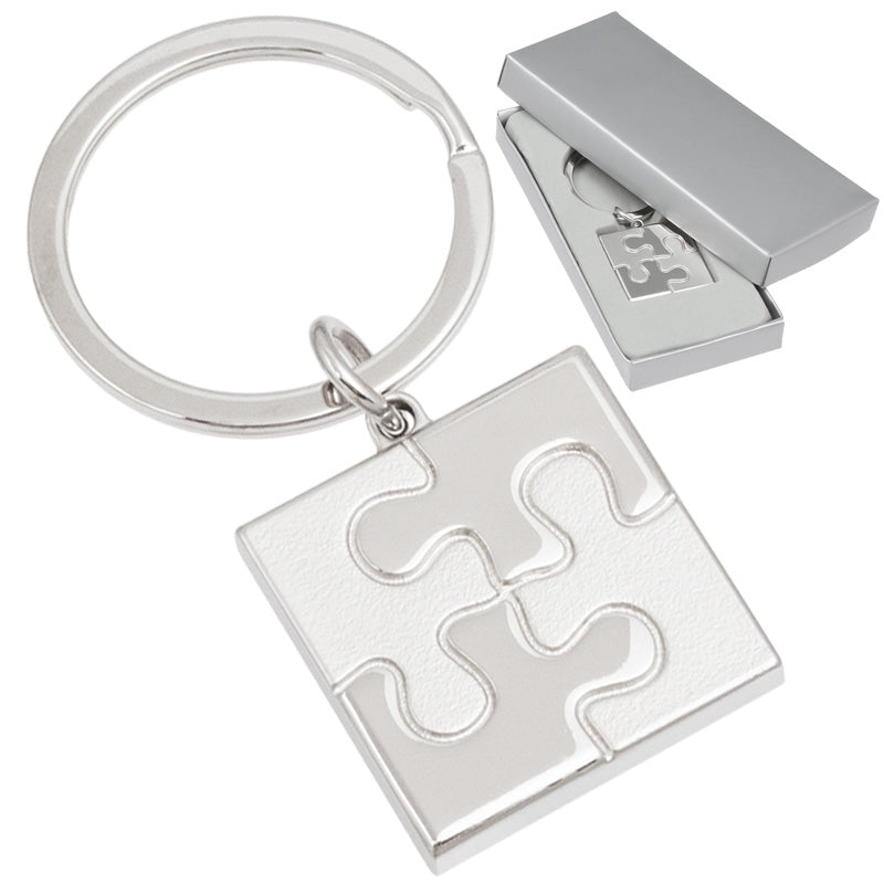 There are two images. On the right, the font of a square keychain with a puzzle piece motif molded within the square. It is displayed in a silver gift box. On the right is the same keychain, zoomed in for clearer detail.