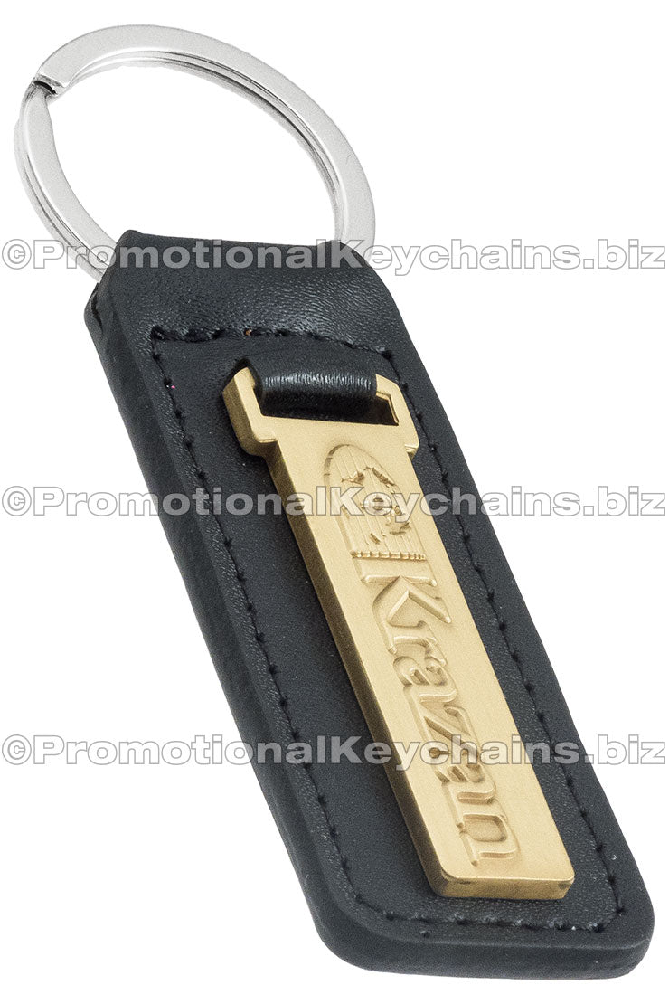 A black leather fob keychain with a rectangular brass attachment that has a logo embossed on the metal.