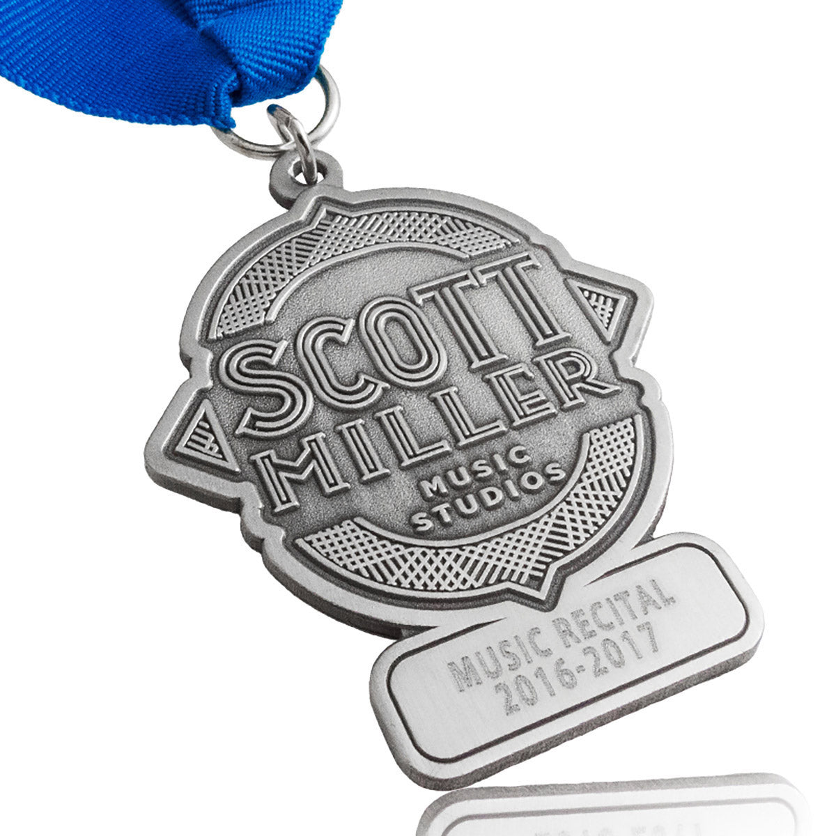 An antiqued nickel medal with blue ribbon, embossed with "Scott Miller Music Studios" in the center and "Music Recital 2016-2017" engraved on the bottom section.