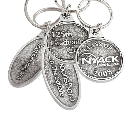 Photos of the front and back of two separate keychains. To the left, an ovular genuine pewter keychain featuring "Inn BoonsBoro On The Square" embossed on the front and and the establishment date embossed on the back. On the right, a circular design with the logo for "NYACK" embossed on the front and "125th Graduating Class" embossed on the back.