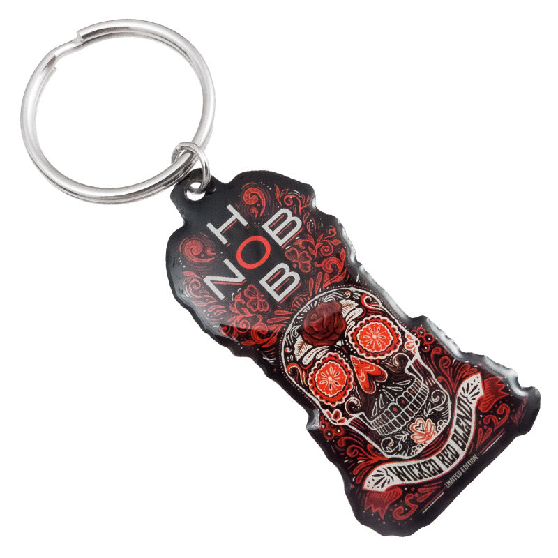 A colorful keychain featuring a skull design, "HOB" and "Wicked Red Blend" text, adorned with floral accents in various shades of red, black, and orange.