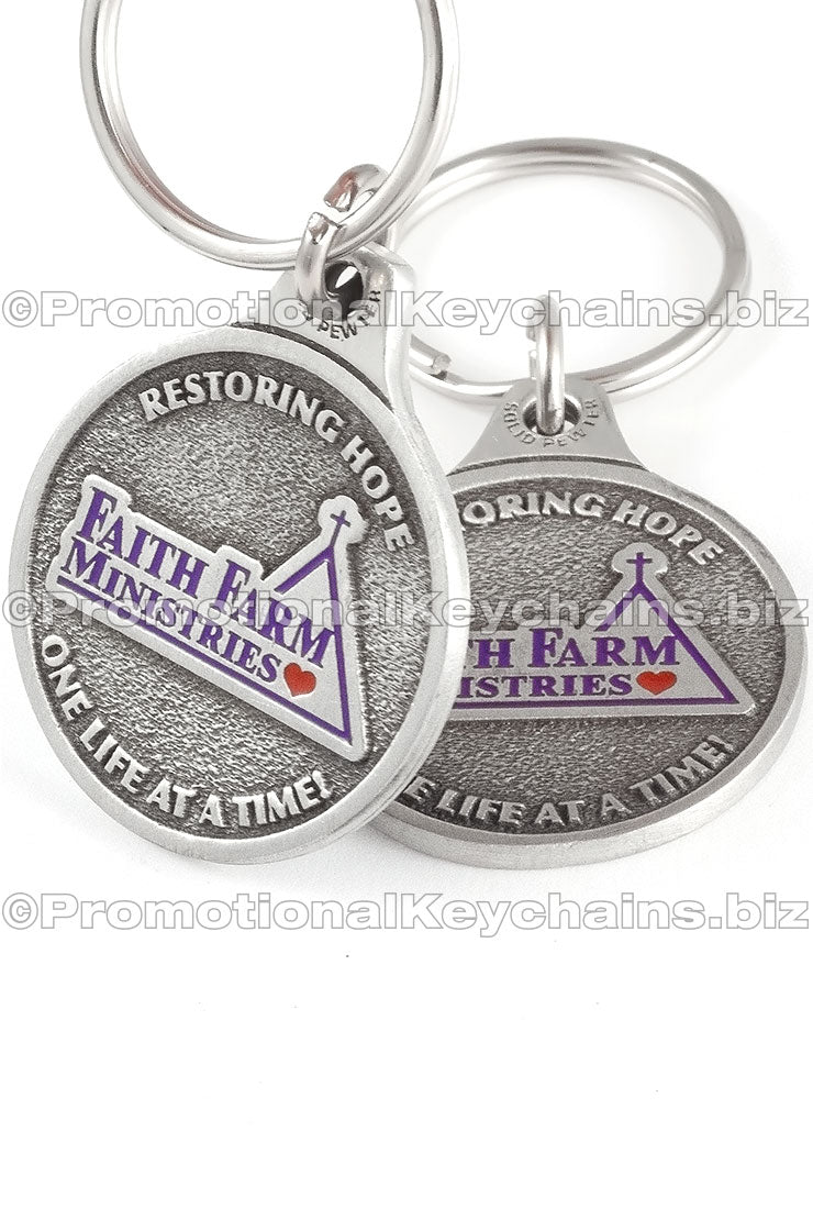 Two angles of the same genuine pewter keychain, circular in shape. It features the logo for "Faith Farm Ministries" in purple and red enamel color.