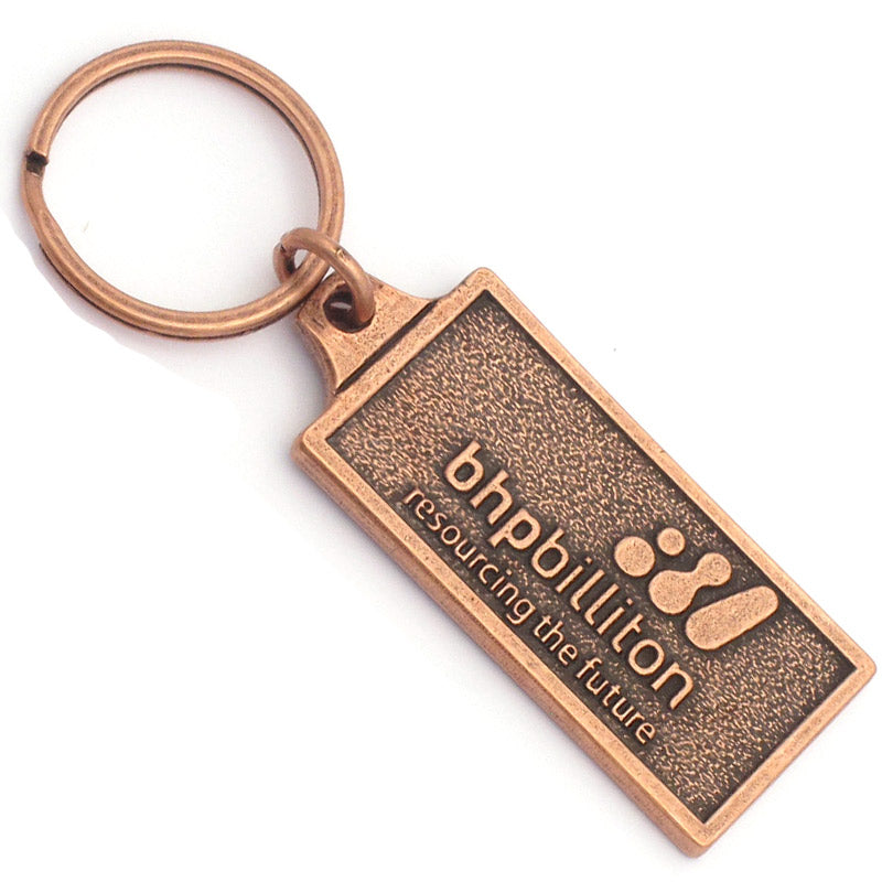 A rectangular antique copper keychain with the logo for BHPBilliton embossed on the front.