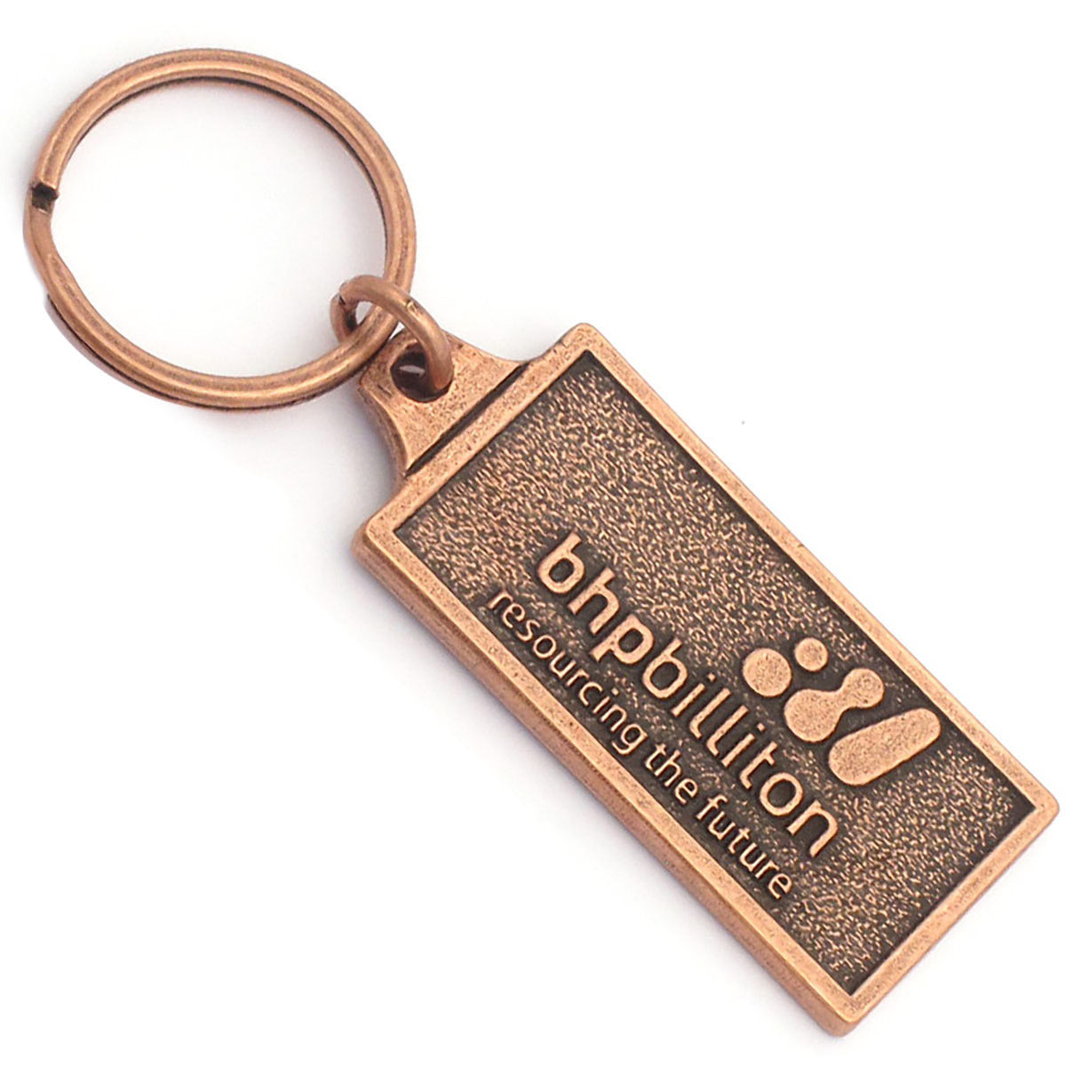 A rectangular antique copper keychain with the logo for BHPBilliton embossed on the front.