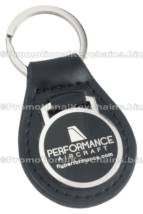 A black leather fob keychain with a polished nickel medallion attached, featuring the logo of Performance Aircraft on a black hard enamel background.