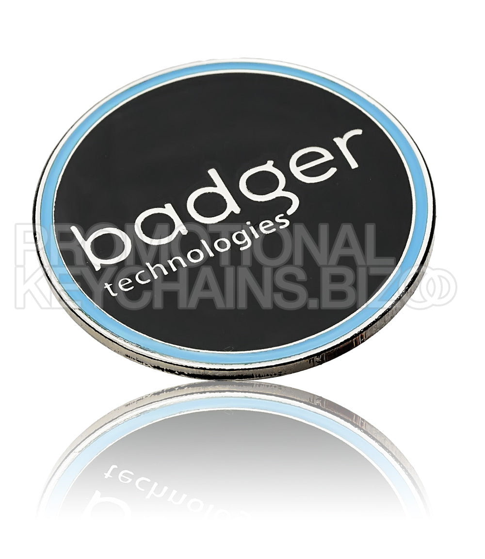 A circular medallion in polished nickel featuring the logo for Badger Technologies centered on a black hard enamel background, bordered by a light blue enamel rim.