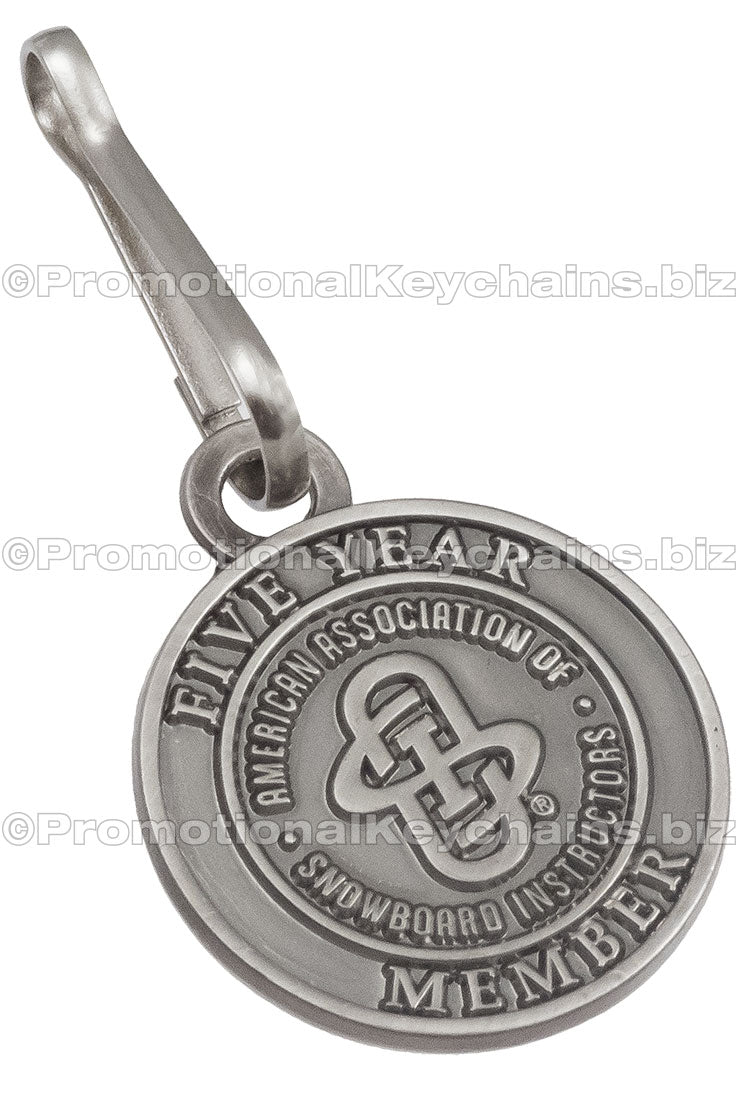 A round, antiqued nickel zipper pull displaying "American Association of Snowboard Instructors" branding.