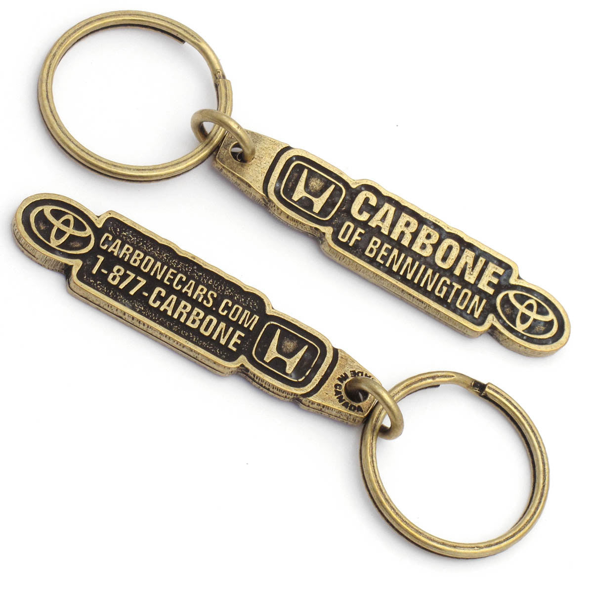 The front and back of the same antiqued brass keychain, featuring "Carbone of Bennington" with the Honda logo on the left and the Toyota logo on the right. The back has a phone number and a website.