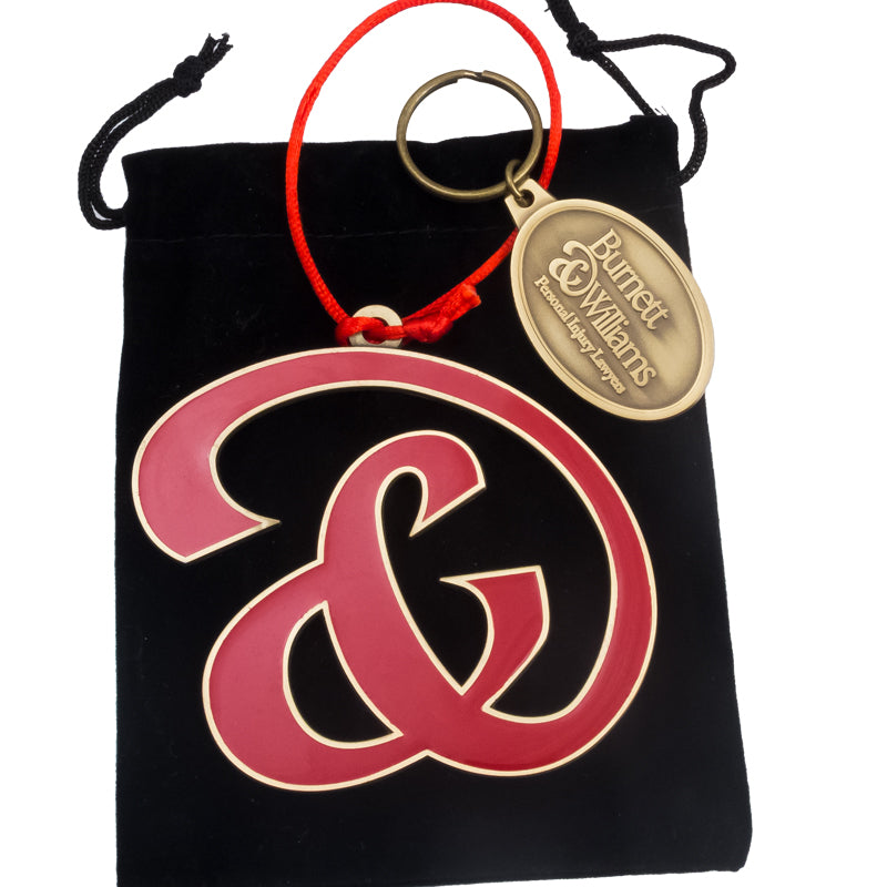 A custom red and gold ornament with a business logo, and matching branded keychain, presented on a black background.