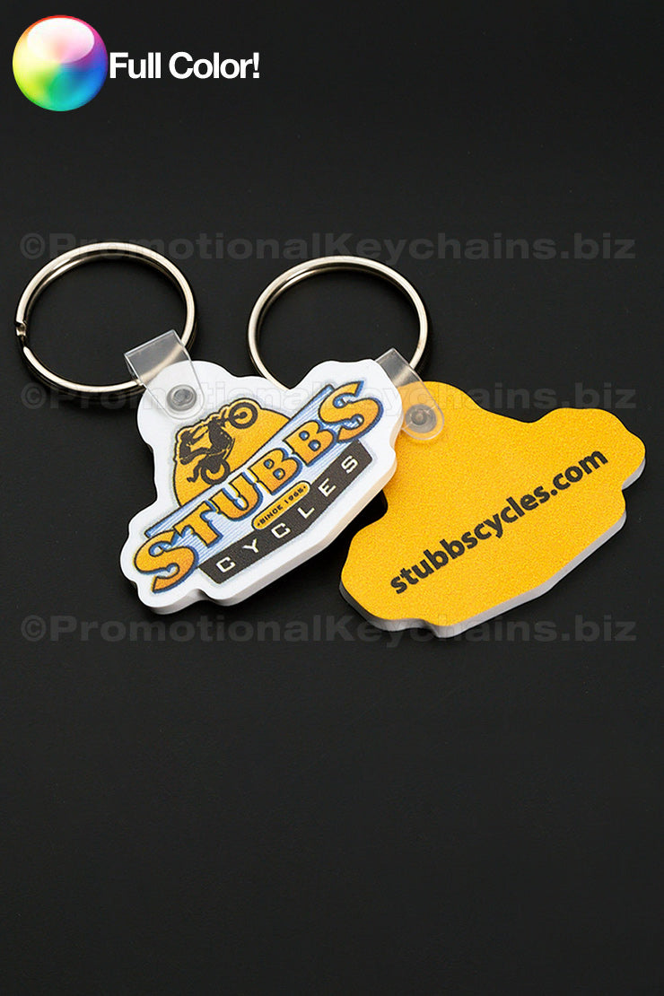 A white and a bright yellow vinyl keychain in the shape of the Stubbs logo with a printing of the logo on the front in full color against a dark background..