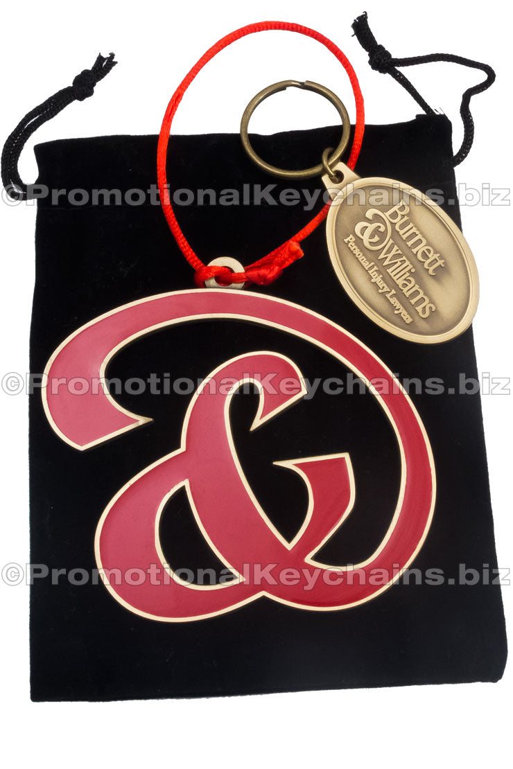 A custom red and gold ornament with a business logo, and matching branded keychain, presented on a black background.