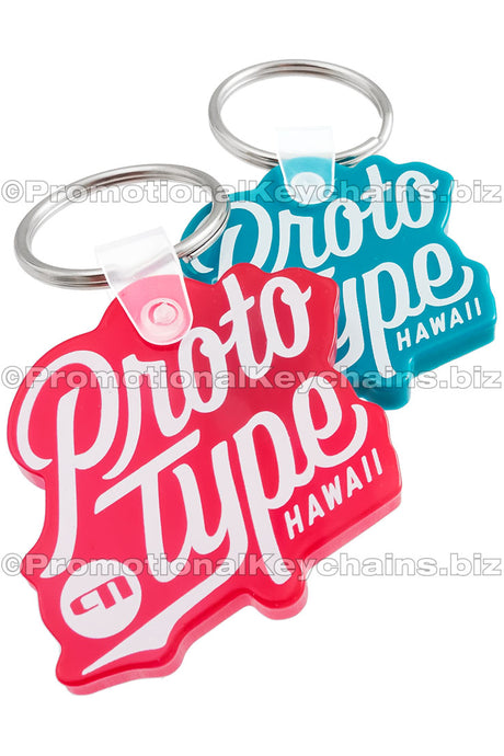 Two vinyl keychains in the shape of the ProtoType logo, in teal, and translucent red vinyl.
