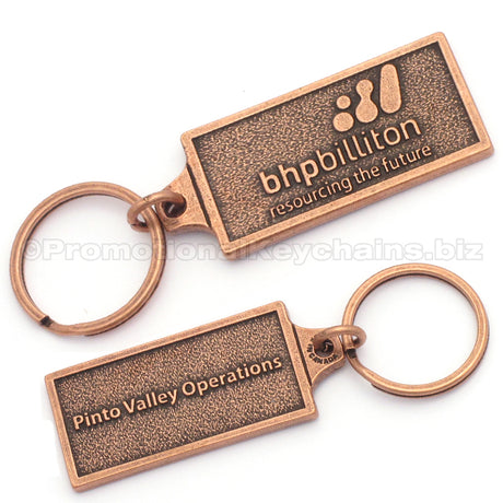 The back and front of a rectangular antique copper keychain. The front has the logo for BHPBilliton embossed, and the back has the text "Pinto Valley Operations" embossed.