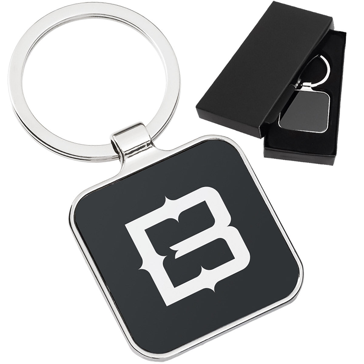 There are two images. On the right, a polished metal keychain featuring a square black background displayed in a black gift box. On the left is the same keychain with a logo clearly engraved in the center.