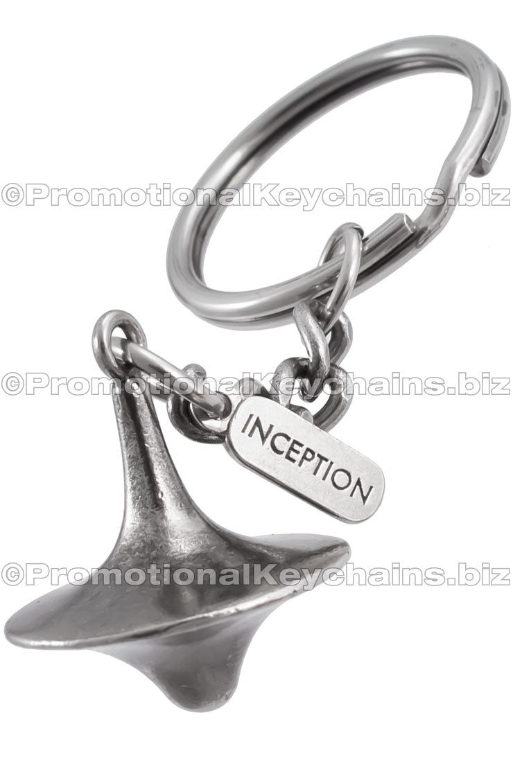 A three-dimensional nickel plated spinning top with an attached tag branded with the "INCEPTION" logo.