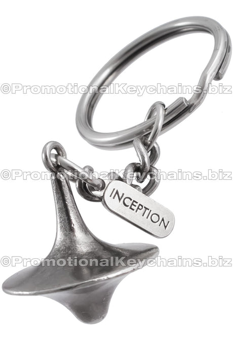 A three-dimensional nickel plated spinning top with an attached tag branded with the "INCEPTION" logo.
