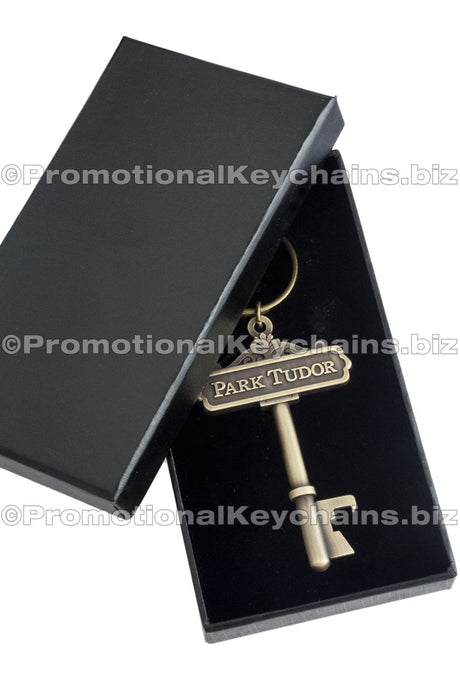 Image shows custom box with lid half open. Antiqued gold key shaped bottle opener inside custom black box.