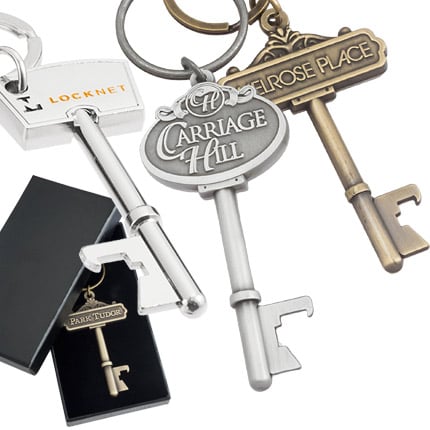 Multiple key shaped bottle opener keychains. Image shows keys in polished nickel, antiqued silver and antiqued gold. Example of custom black box in background.