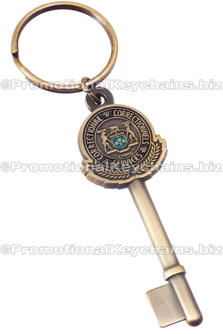 An antiqued brass keychain shaped like a key with a circular Ontario Correctional Services emblem embossed on the bow.