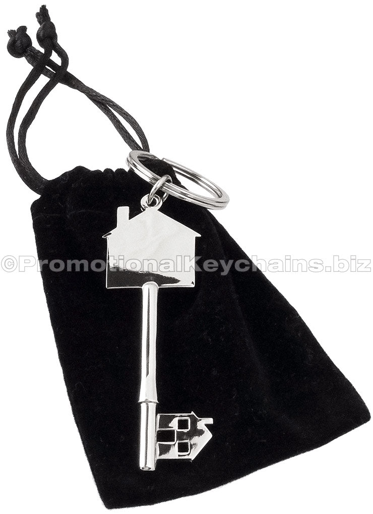 A polished key-shaped keychain featuring a house silhouette, resting on top of a black velvet drawstring bag.