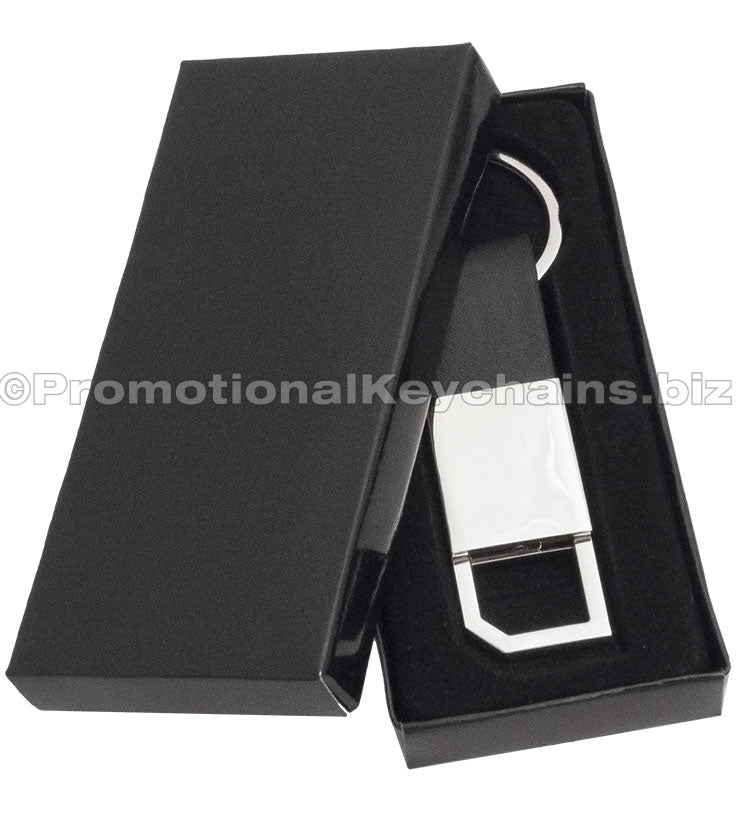 A polished metal keychain with a leather strap and a pull and twist feature on the other end displayed in a black gift box.