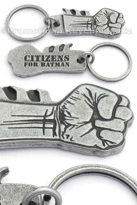Multiple photos of an antiqued nickel keychain featuring a clenched fist design on the front with "Citizens for Batman" debossed on the backside.